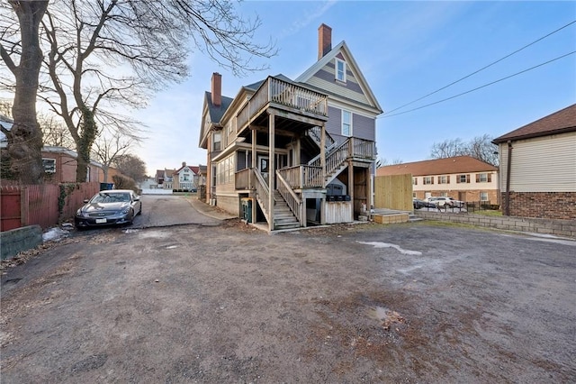 view of front facade featuring aphalt driveway, a chimney, stairs, and fence