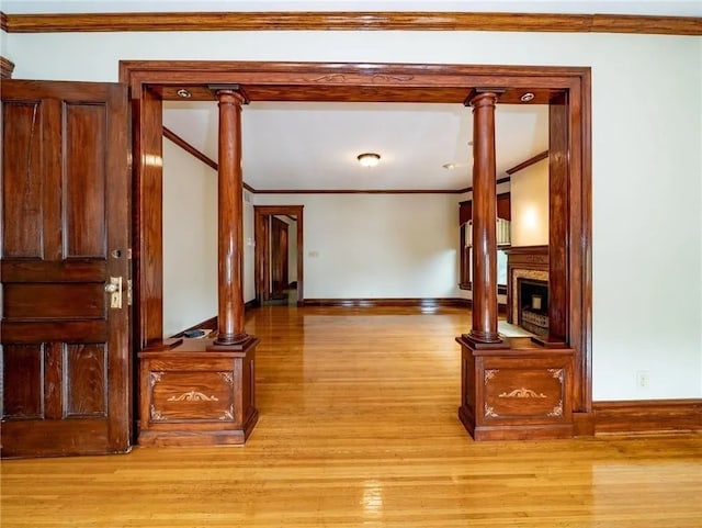 hall featuring light wood-style flooring, decorative columns, baseboards, and ornamental molding