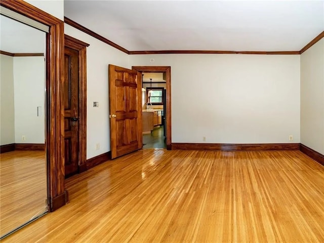 spare room with crown molding, baseboards, and light wood-type flooring