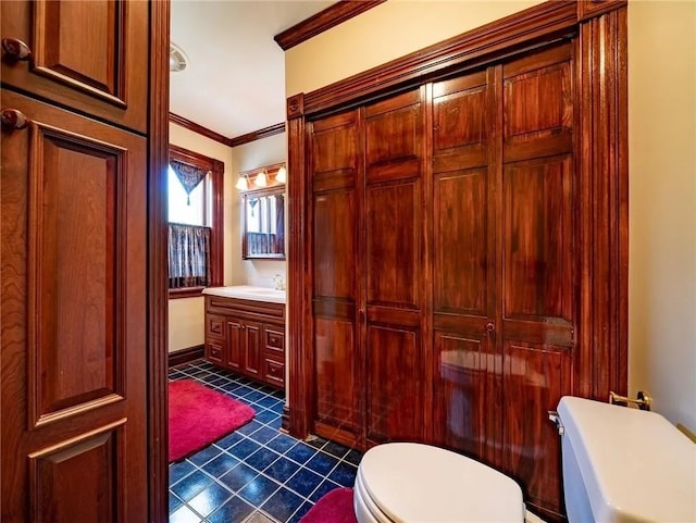 half bath with tile patterned floors, vanity, toilet, and crown molding