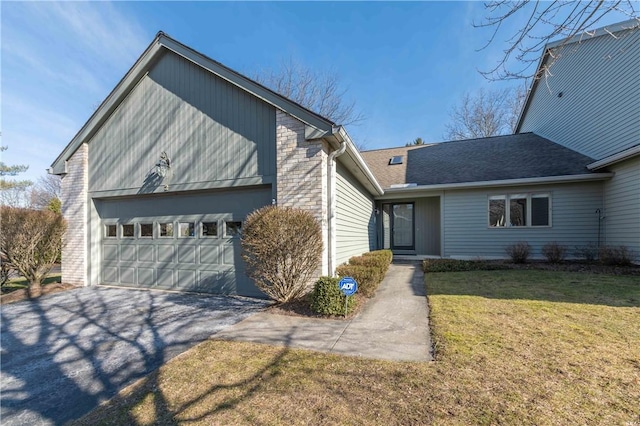 view of front of home with aphalt driveway, an attached garage, brick siding, and a front lawn