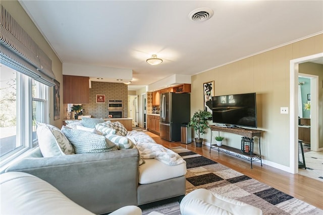 living room with visible vents, baseboards, light wood-style floors, crown molding, and a brick fireplace