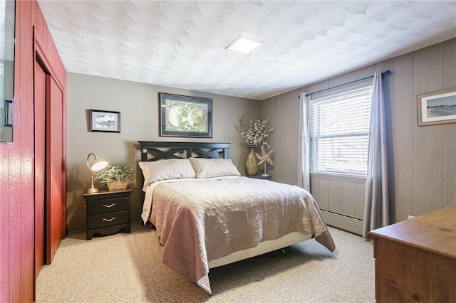 bedroom with light carpet, wood walls, a baseboard heating unit, and a closet