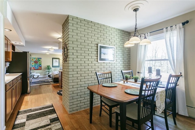 dining area with an accent wall, light wood-type flooring, and brick wall