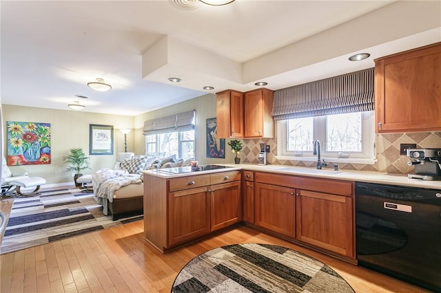 kitchen with black appliances, a sink, open floor plan, light wood finished floors, and light countertops