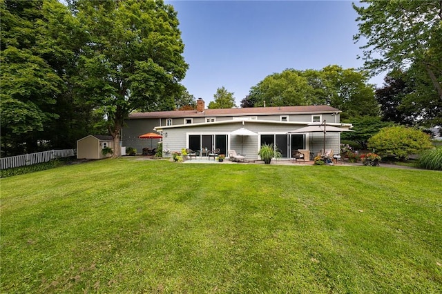 rear view of property featuring a storage unit, fence, a yard, an outdoor structure, and a patio area