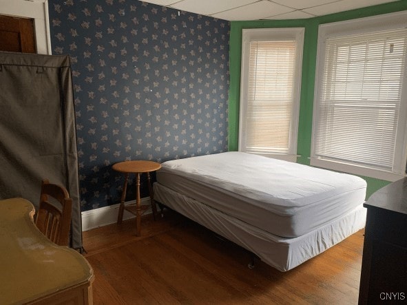 bedroom with wallpapered walls, wood finished floors, and baseboards