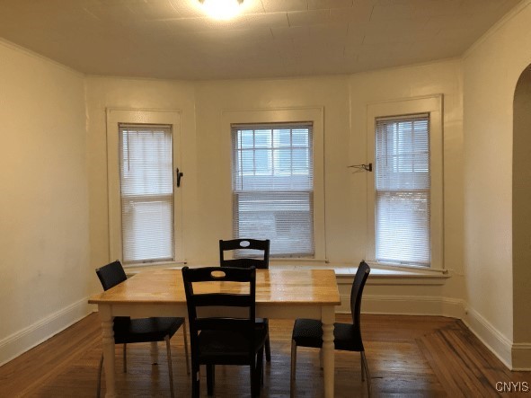 dining space with baseboards, arched walkways, and wood finished floors