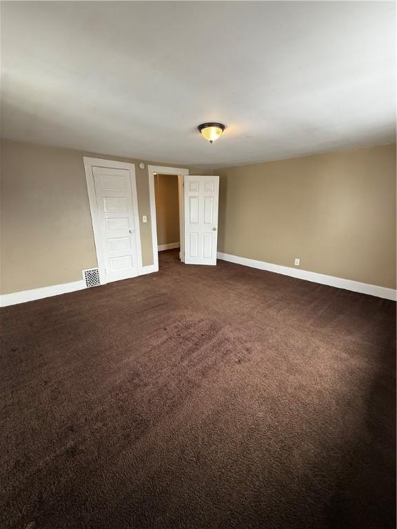 spare room featuring visible vents, baseboards, and dark colored carpet