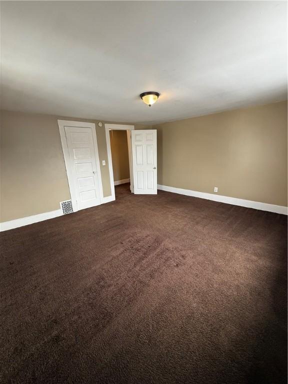 spare room with dark colored carpet, visible vents, and baseboards