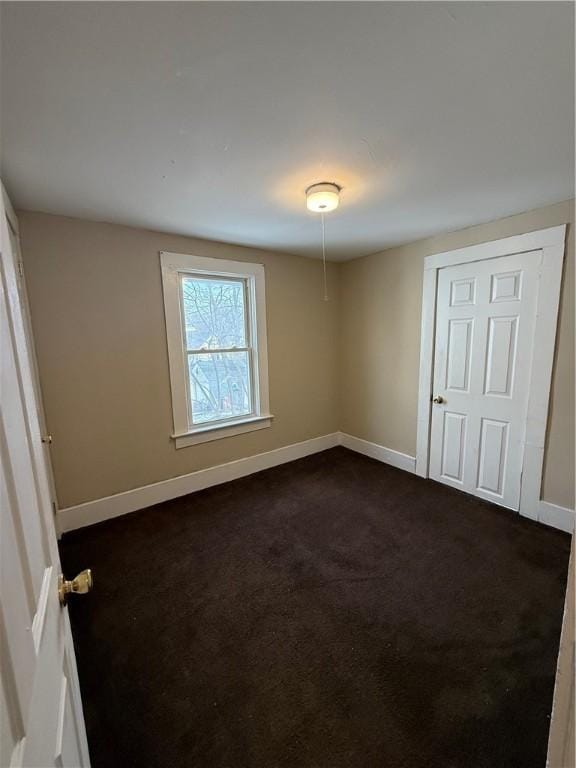 unfurnished bedroom featuring baseboards and dark carpet