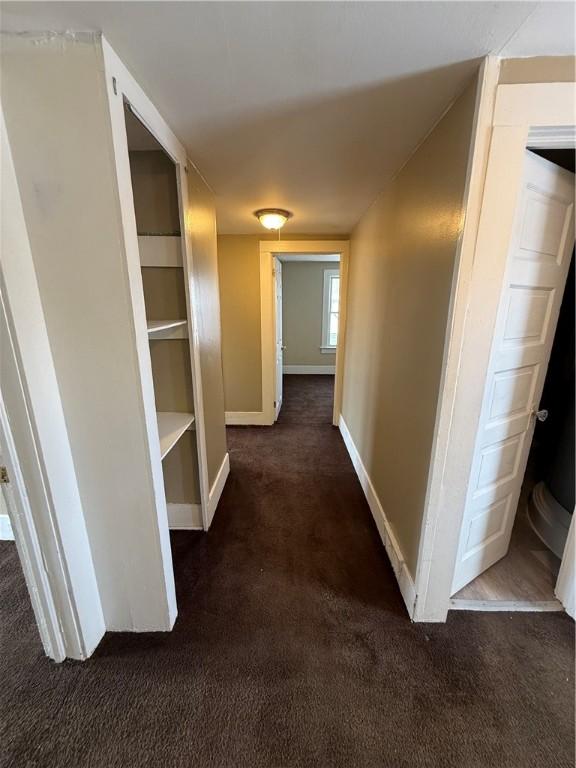 hallway with dark carpet and baseboards