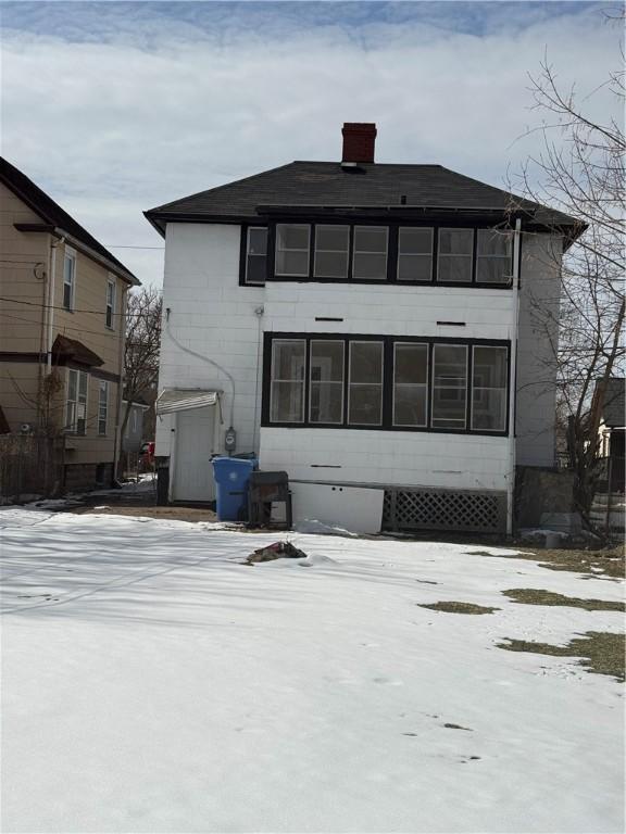 snow covered rear of property with a chimney