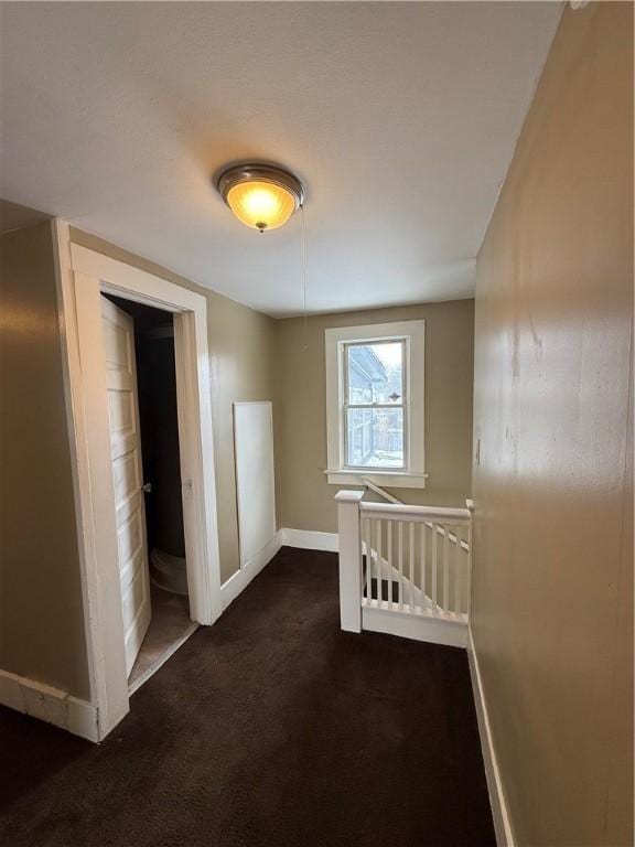 corridor featuring an upstairs landing, baseboards, and dark colored carpet