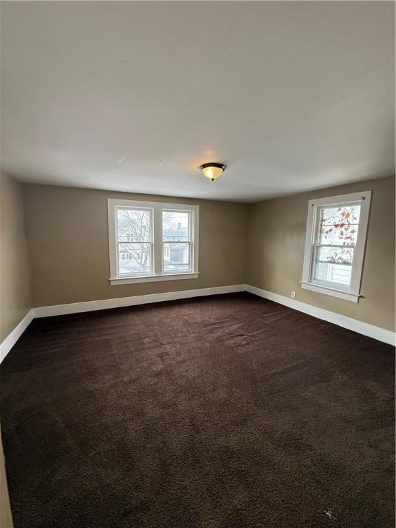 spare room featuring baseboards and dark colored carpet