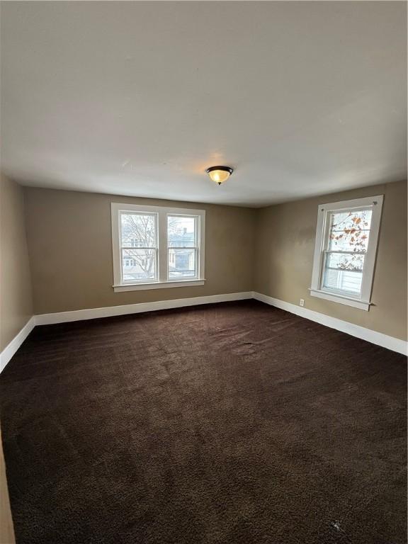 unfurnished room with baseboards and dark colored carpet