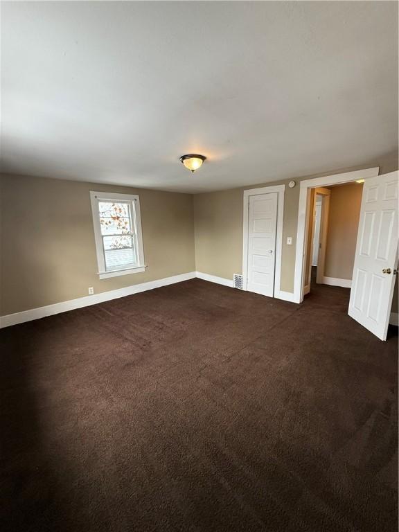 spare room featuring visible vents, baseboards, and dark carpet