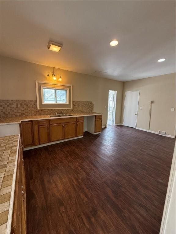 kitchen featuring tile countertops, dark wood-style flooring, a sink, brown cabinets, and backsplash