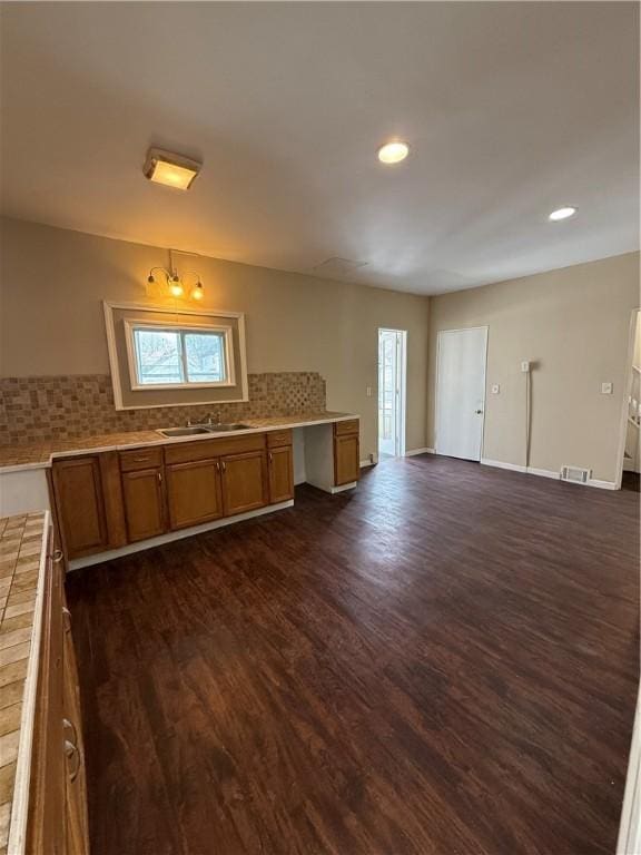 kitchen with a sink, baseboards, decorative backsplash, brown cabinetry, and dark wood-style flooring