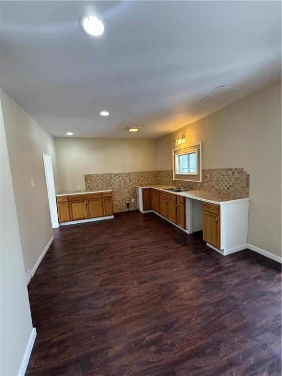 kitchen featuring brown cabinets, dark wood-type flooring, backsplash, light countertops, and baseboards