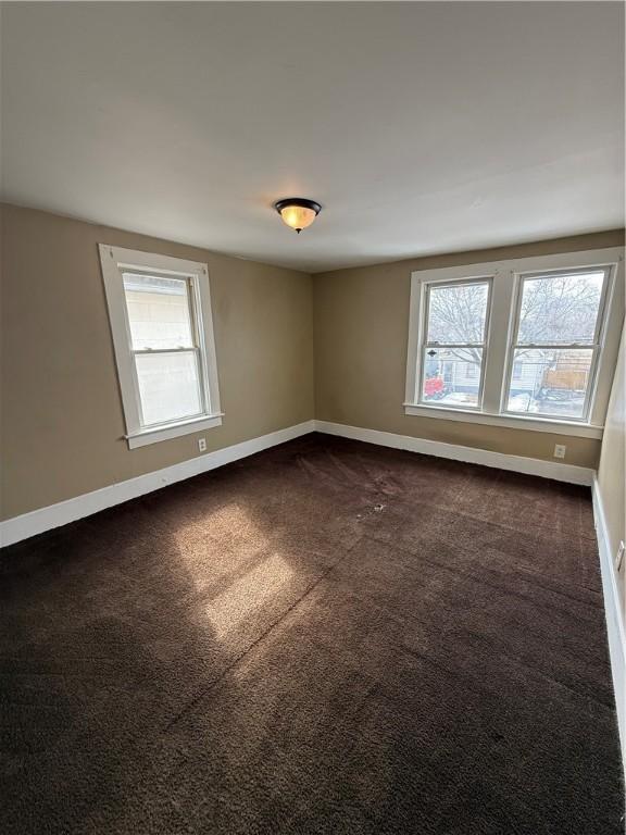 empty room with baseboards and dark colored carpet