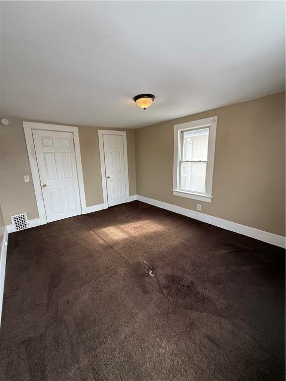 unfurnished bedroom featuring visible vents, baseboards, and dark carpet