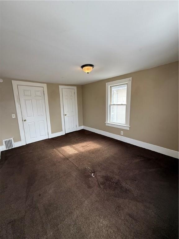 unfurnished bedroom featuring visible vents, baseboards, and dark carpet