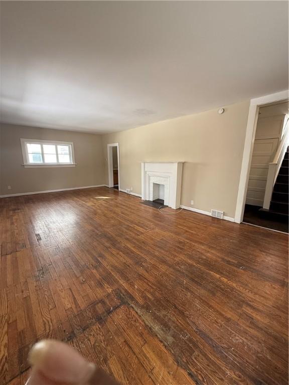 unfurnished living room featuring visible vents, dark wood-type flooring, baseboards, stairs, and a fireplace