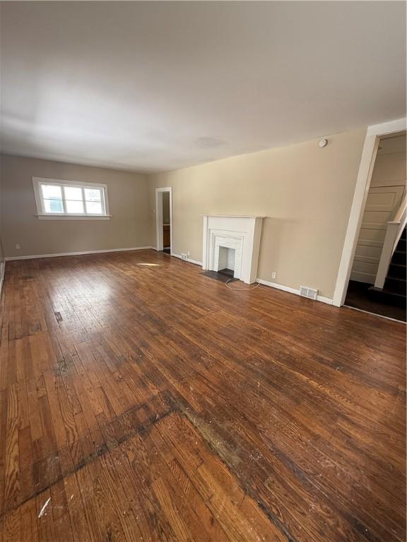 unfurnished living room with hardwood / wood-style floors, a fireplace with flush hearth, baseboards, and visible vents