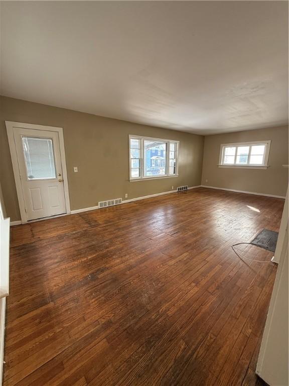 empty room featuring dark wood-style floors, visible vents, a wealth of natural light, and baseboards