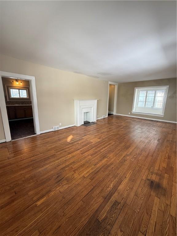 unfurnished living room featuring visible vents, a fireplace, baseboards, and wood-type flooring