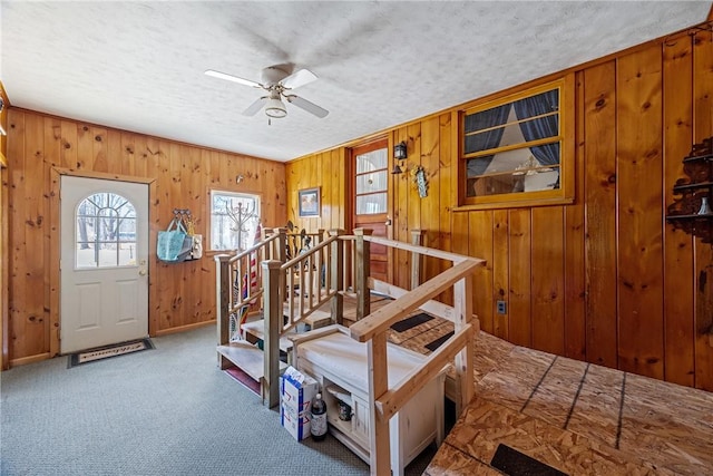 foyer entrance featuring ceiling fan, carpet flooring, wood walls, and a textured ceiling