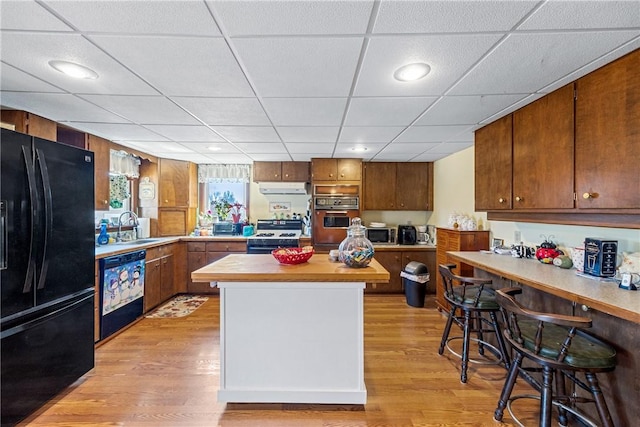 kitchen featuring a sink, light wood-type flooring, black appliances, and under cabinet range hood