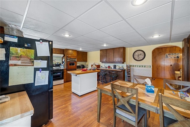 kitchen featuring under cabinet range hood, gas range oven, freestanding refrigerator, wall oven, and light wood finished floors