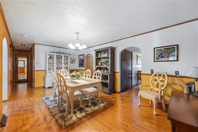 dining area with an inviting chandelier, light wood-style flooring, arched walkways, and a textured ceiling