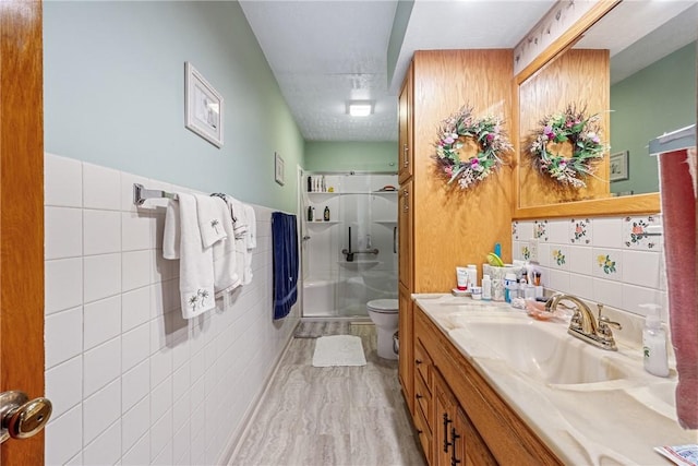 full bathroom with toilet, a stall shower, tile walls, wainscoting, and vanity