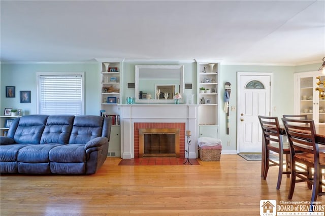 living room featuring crown molding, a brick fireplace, wood finished floors, and baseboards