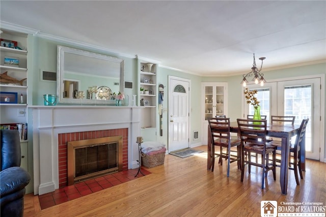 dining space featuring french doors, a brick fireplace, wood finished floors, and ornamental molding