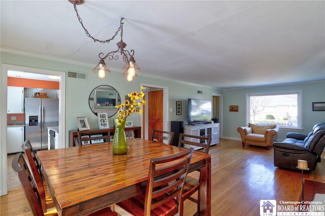 dining room featuring visible vents, light wood-style flooring, and crown molding