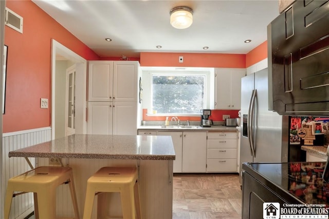 kitchen featuring a wainscoted wall, visible vents, a sink, black range with electric cooktop, and white cabinetry