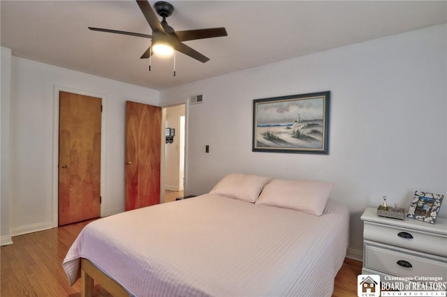 bedroom with a ceiling fan, wood finished floors, visible vents, and baseboards