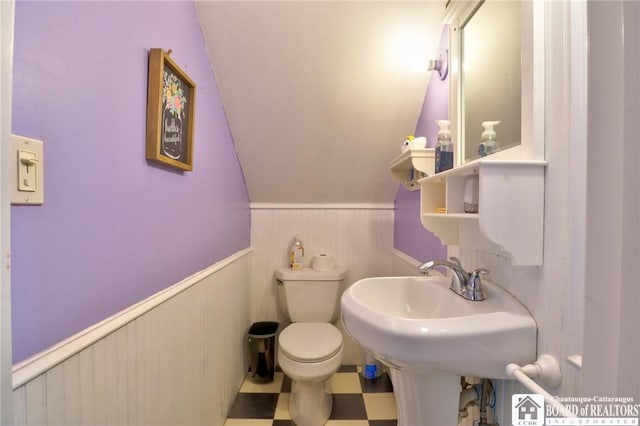 half bath featuring tile patterned floors, a wainscoted wall, lofted ceiling, and toilet