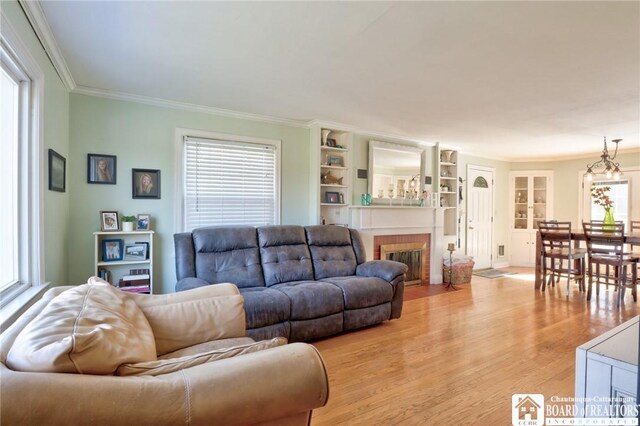 living area featuring plenty of natural light, light wood-style flooring, a fireplace, and ornamental molding