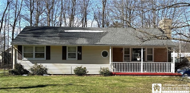 view of front of house featuring a chimney, roof with shingles, covered porch, and a front yard