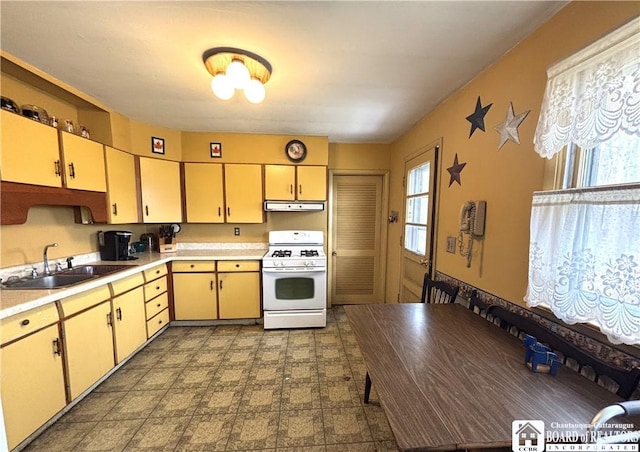 kitchen featuring a healthy amount of sunlight, white gas stove, a sink, light countertops, and under cabinet range hood