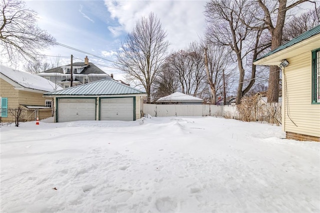 yard layered in snow with a garage, an outbuilding, and fence