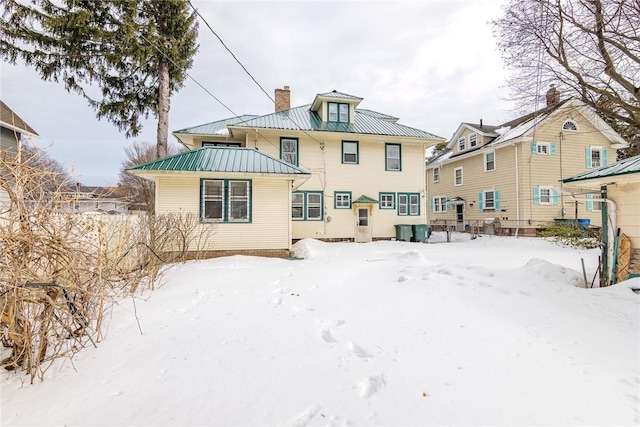 snow covered house with metal roof, a chimney, and a standing seam roof