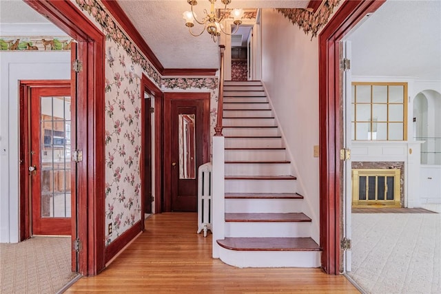 stairway featuring a textured ceiling, wood finished floors, crown molding, and wallpapered walls