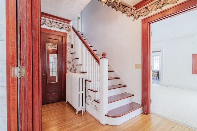 staircase with radiator, wood finished floors, and a textured ceiling