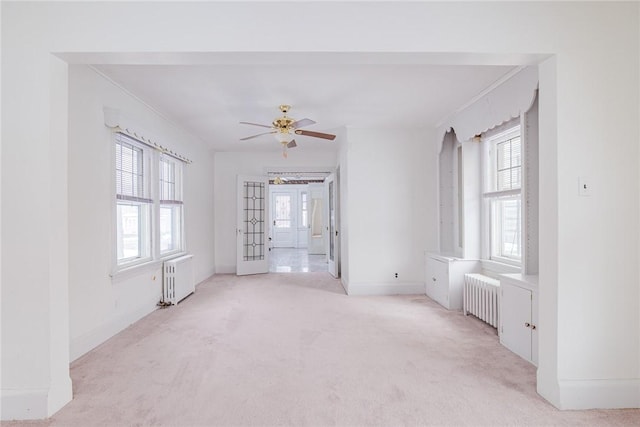 empty room with radiator, baseboards, light colored carpet, radiator heating unit, and a ceiling fan